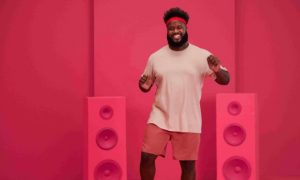 Dark-haired man laughing between two horns pink background
