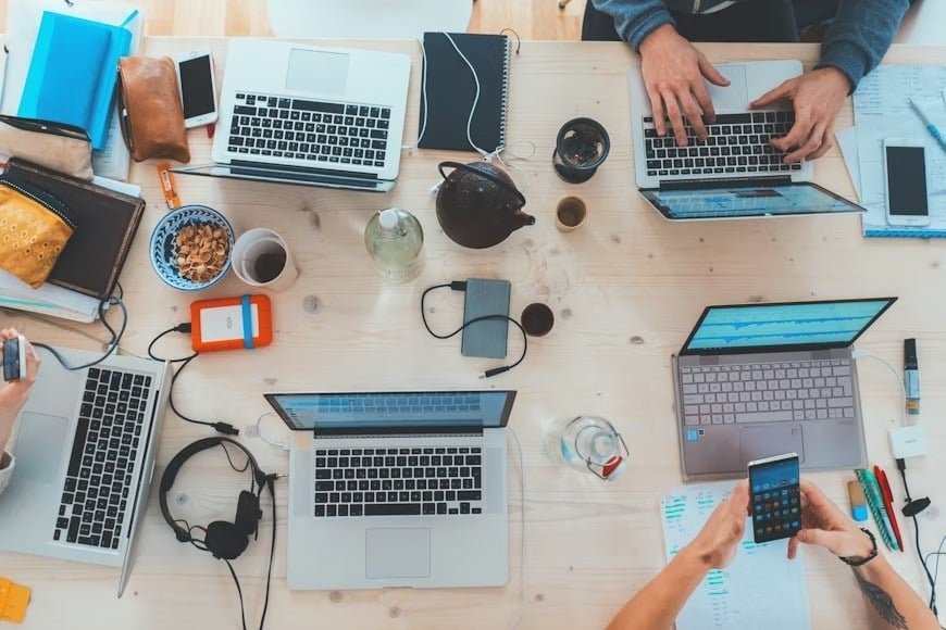 Aerial view of five laptops opened on a table, with three being used for content creation.