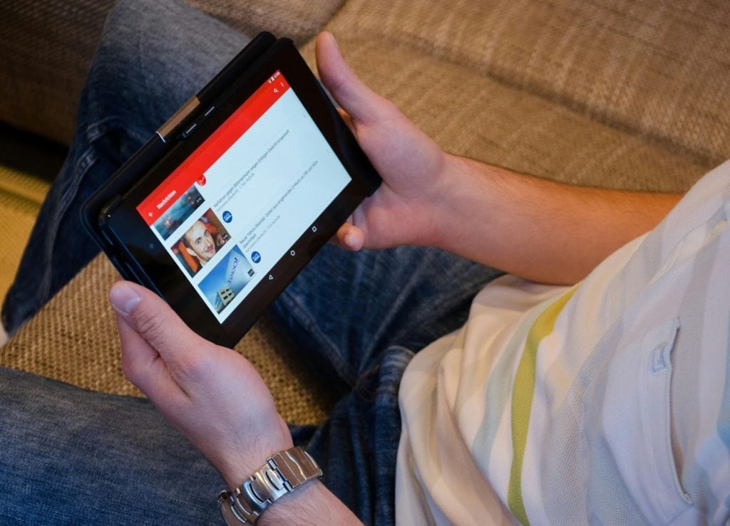 Person holding tablet to watch videos, with thumbnails showing on the screen