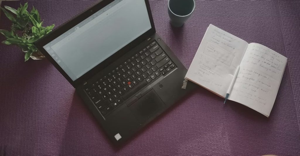 A laptop and an open notebook on a purple background.