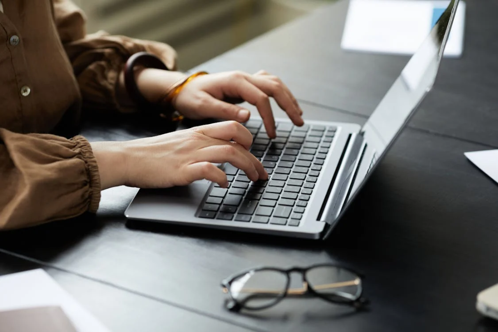 Person typing on a laptop at a dark desk, glasses set aside, representing the unseen effort behind shaping online narratives.