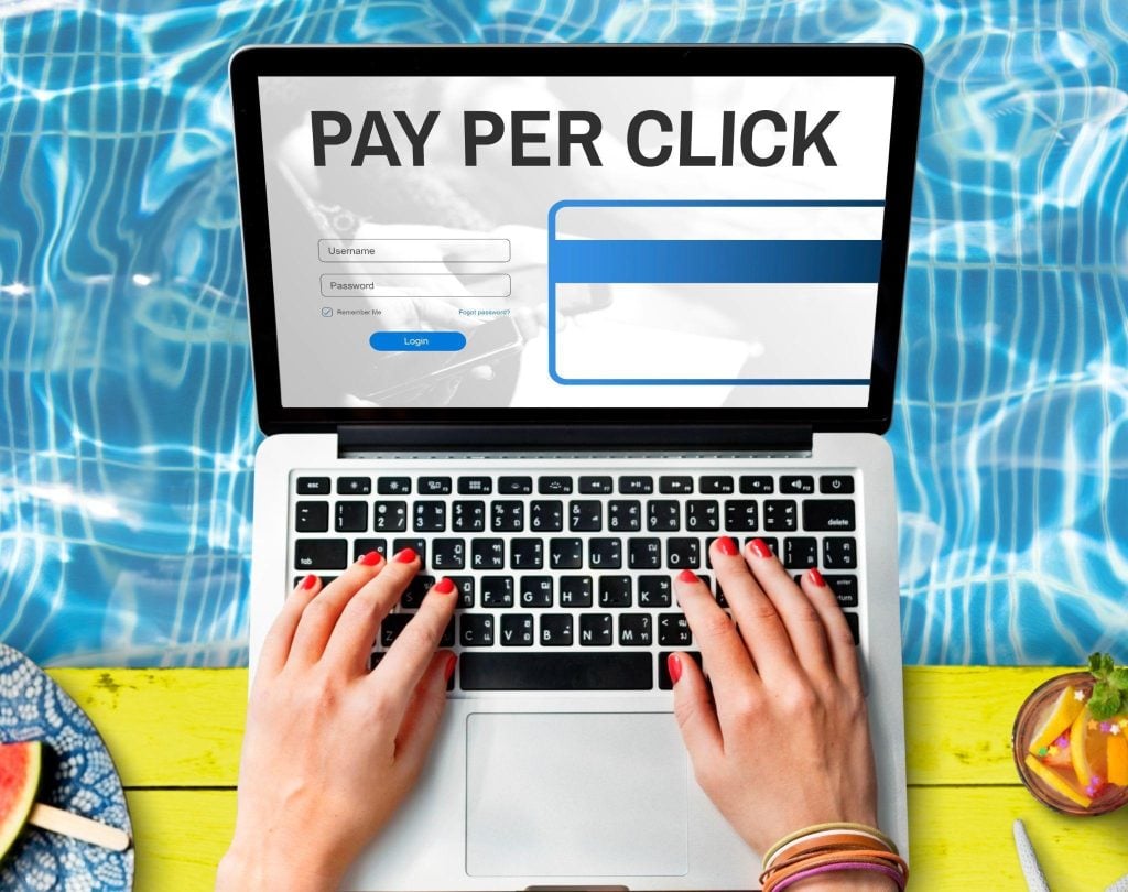 Person typing on a laptop showing a pay-per-click dashboard by a poolside