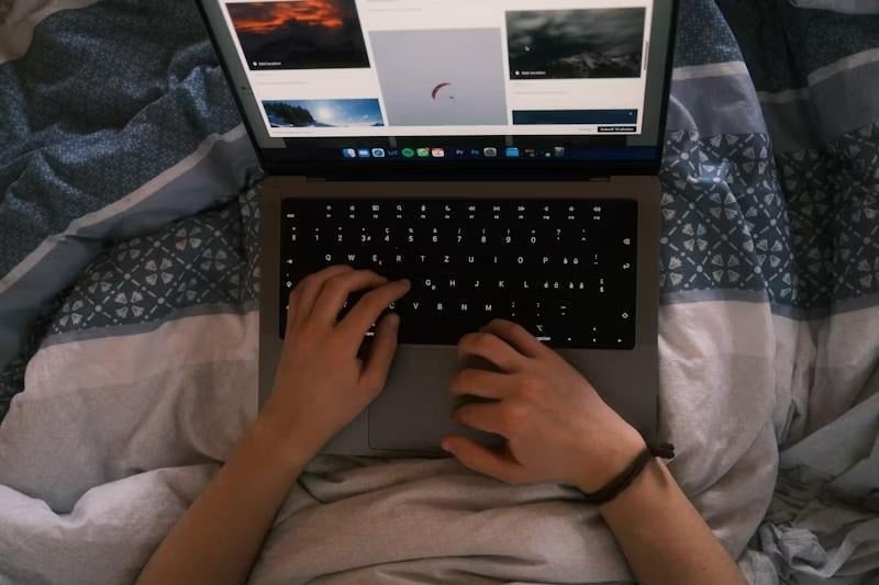 A close up of a person typing on a laptop while laying on a bed.