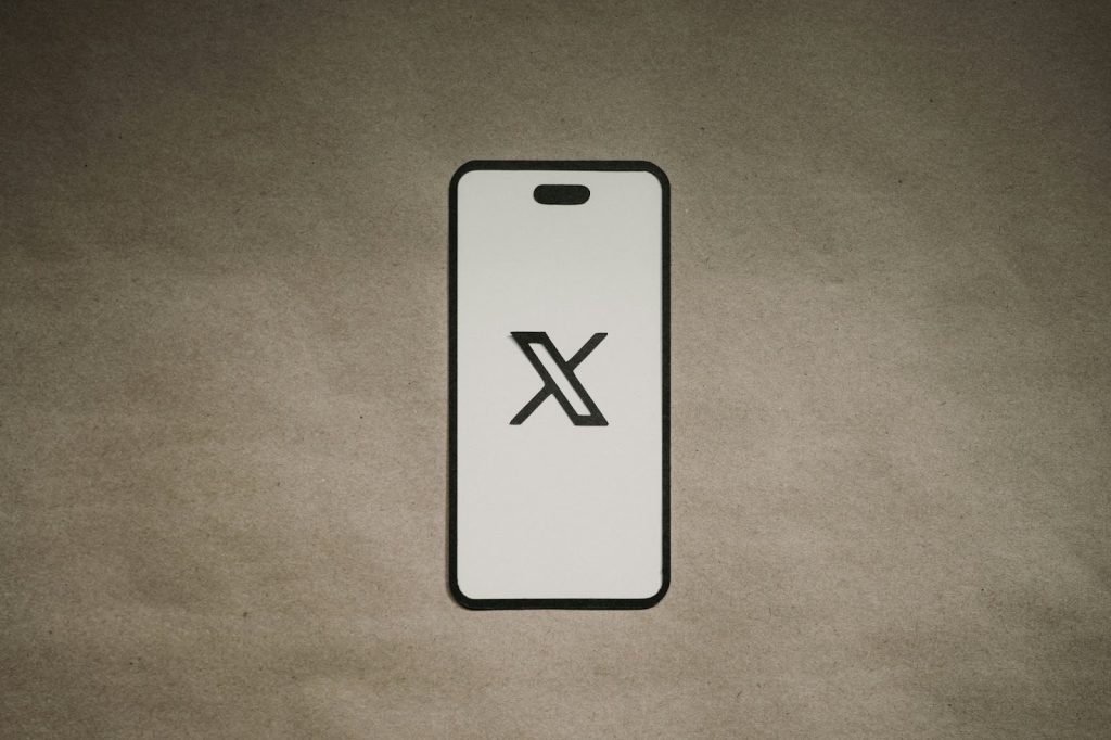 X logo displaying on a mobile phone placed on a cement surface