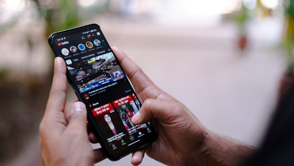 A person holding a smartphone displaying the YouTube app with the Shorts section open.