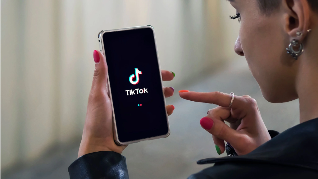 Person with colorful nails holding a smartphone displaying the TikTok logo loading screen.