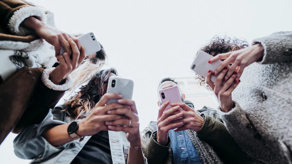 Four people huddled in a circle, each focused on their smartphones, shot from a low angle.