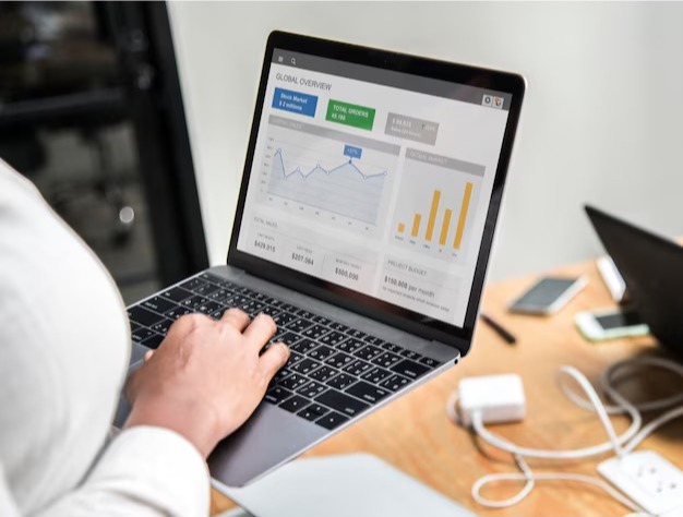 Person typing on a laptop displaying a business analytics dashboard with sales figures, a line graph, and a bar chart.