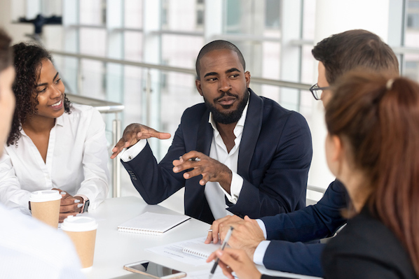 Business professional leading a B2B sales discussion with a team around a conference table.